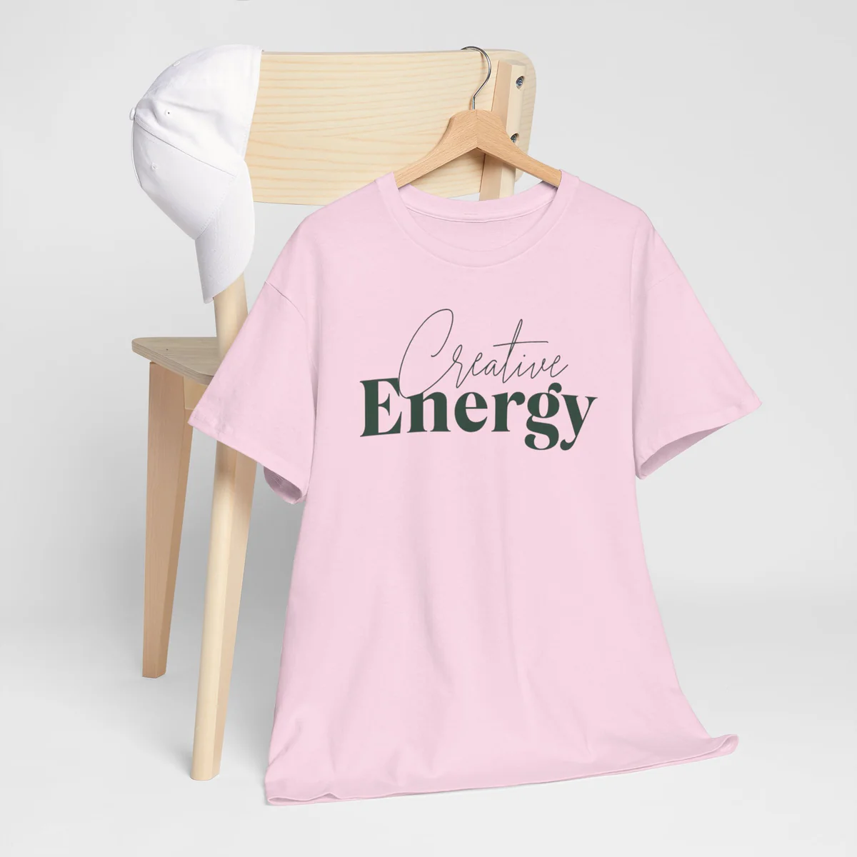 Pink t-shirt with Creative Energy script and bold serif lettering on a wooden hanger